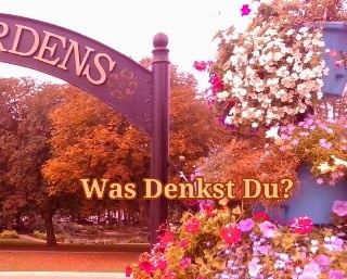 Gardens sign cut off to read as dens next to flowers and trees, caption Was denkst du