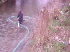 man in waders struggling with large hose and reeds