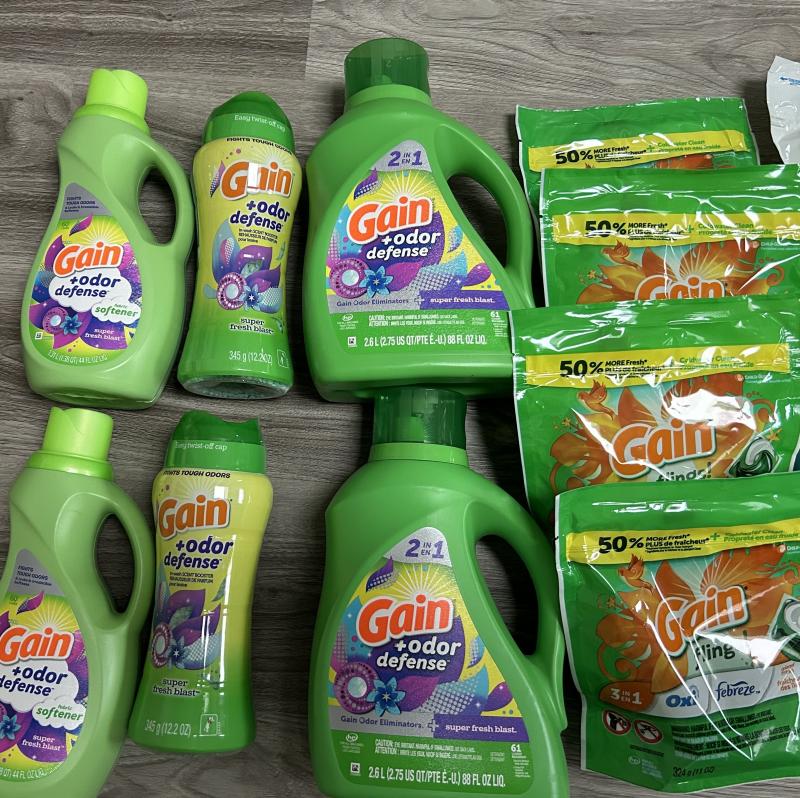 gain +odor defense laundry haul with liquid detergent, fabric softener, scent booster beads, and gain flings pods in super fresh blast scent arranged on wood flooring