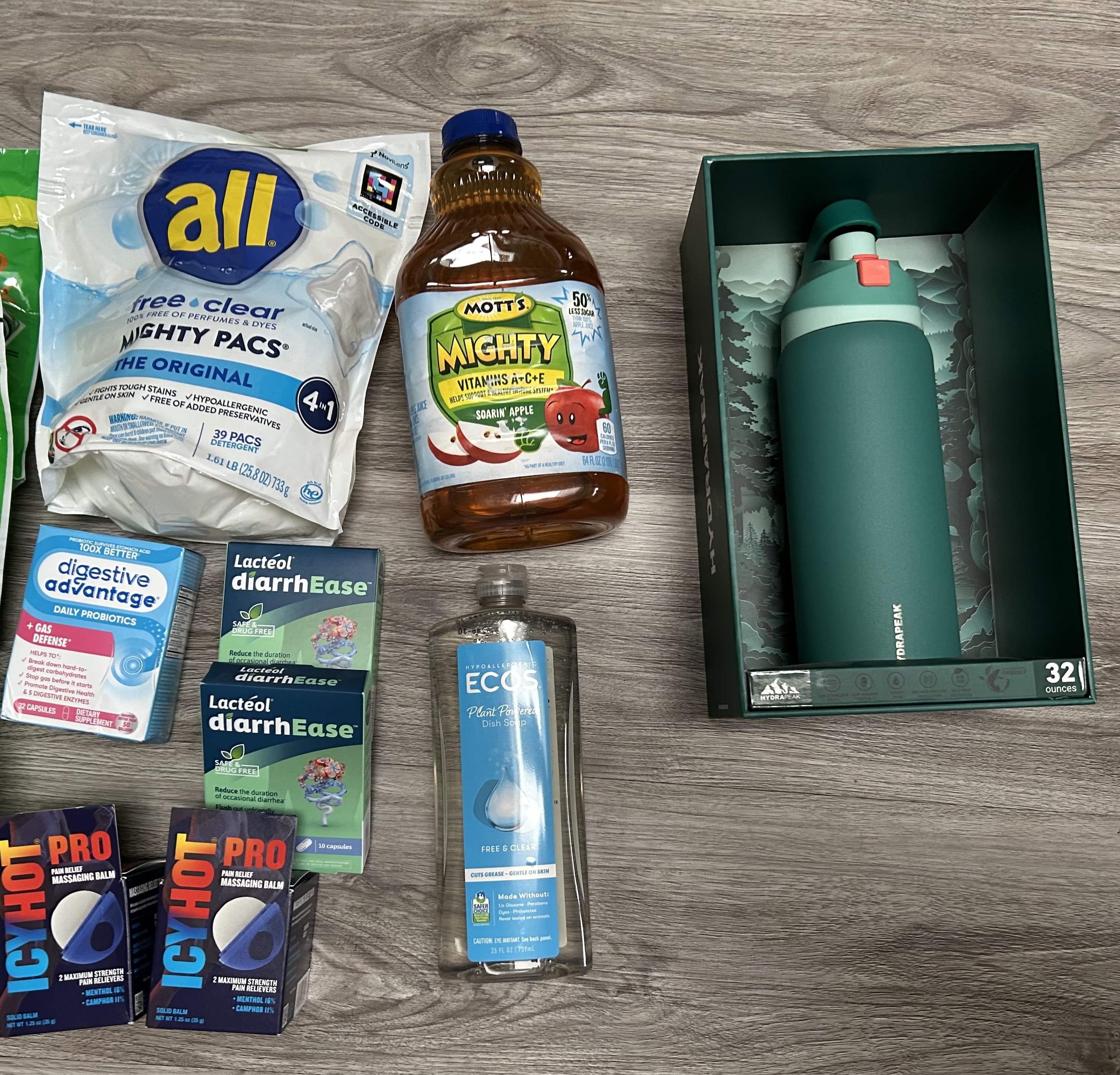 cvs haul with all free clear mighty packs detergent, mott’s mighty apple juice, digestive advantage probiotics, lactéol diarrhease capsules, icy hot pro pain relief balm, ecos free & clear dish soap, and a green hydrapeak 32 oz insulated water bottle on wood flooring