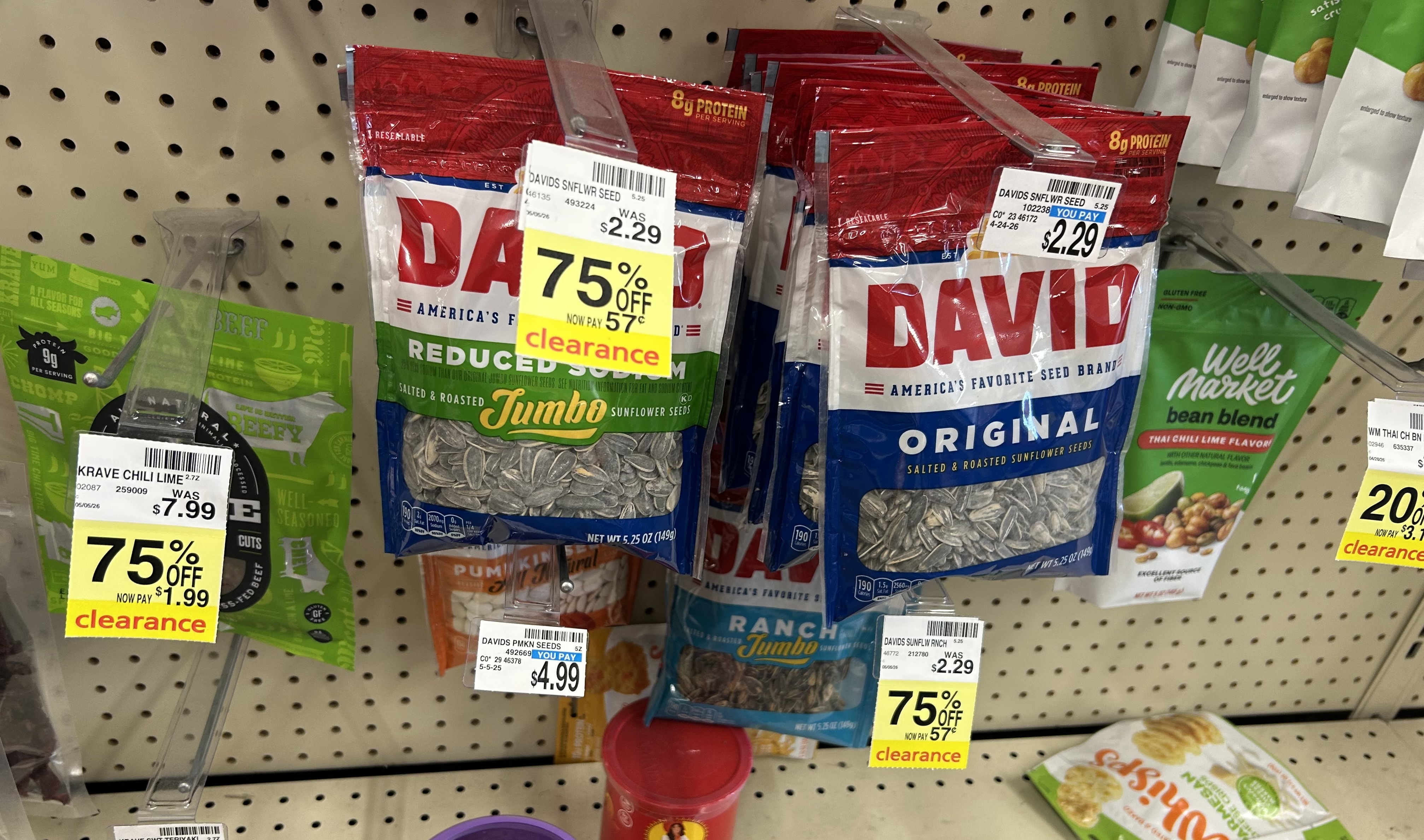store shelf with david jumbo sunflower seeds in reduced sodium, original, and ranch flavors marked 75% off clearance at 57¢, alongside krave chili lime beef cuts and well market thai chili lime bean blend snacks with additional clearance tags visible