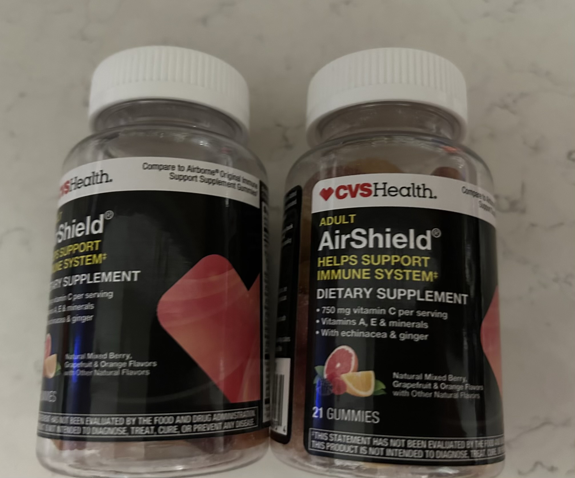 Two bottles of CVS Health Adult AirShield dietary supplements, labeled to help support the immune system with 750 mg vitamin C, vitamins A and E, minerals, echinacea, and ginger. Each bottle contains 21 gummies in natural mixed berry, grapefruit, and orange flavors.