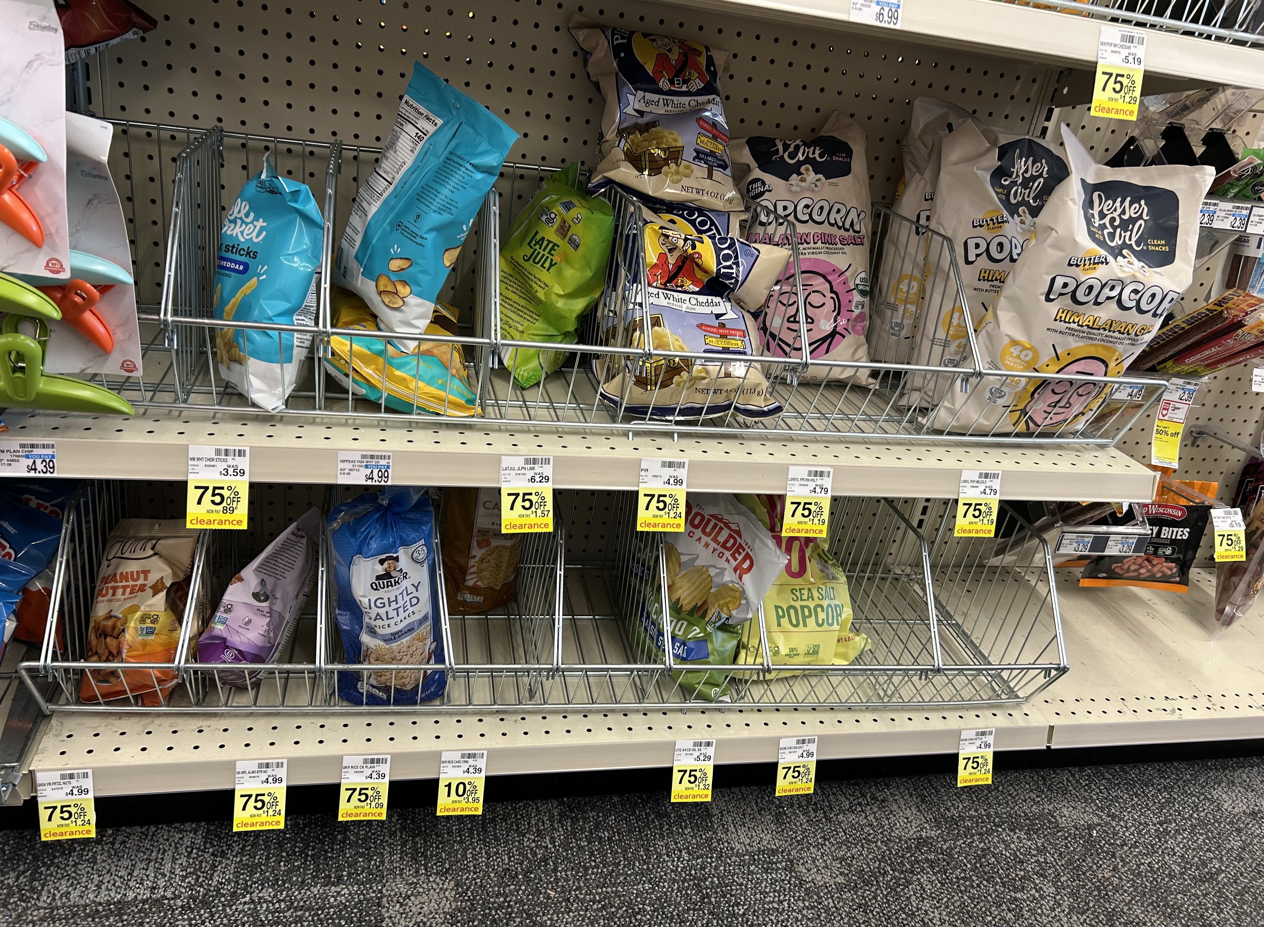 store snack aisle with multiple bags of popcorn, pretzels, chips, and rice cakes marked with yellow clearance tags showing discounts of 75% off and 70% off on various items throughout the shelves