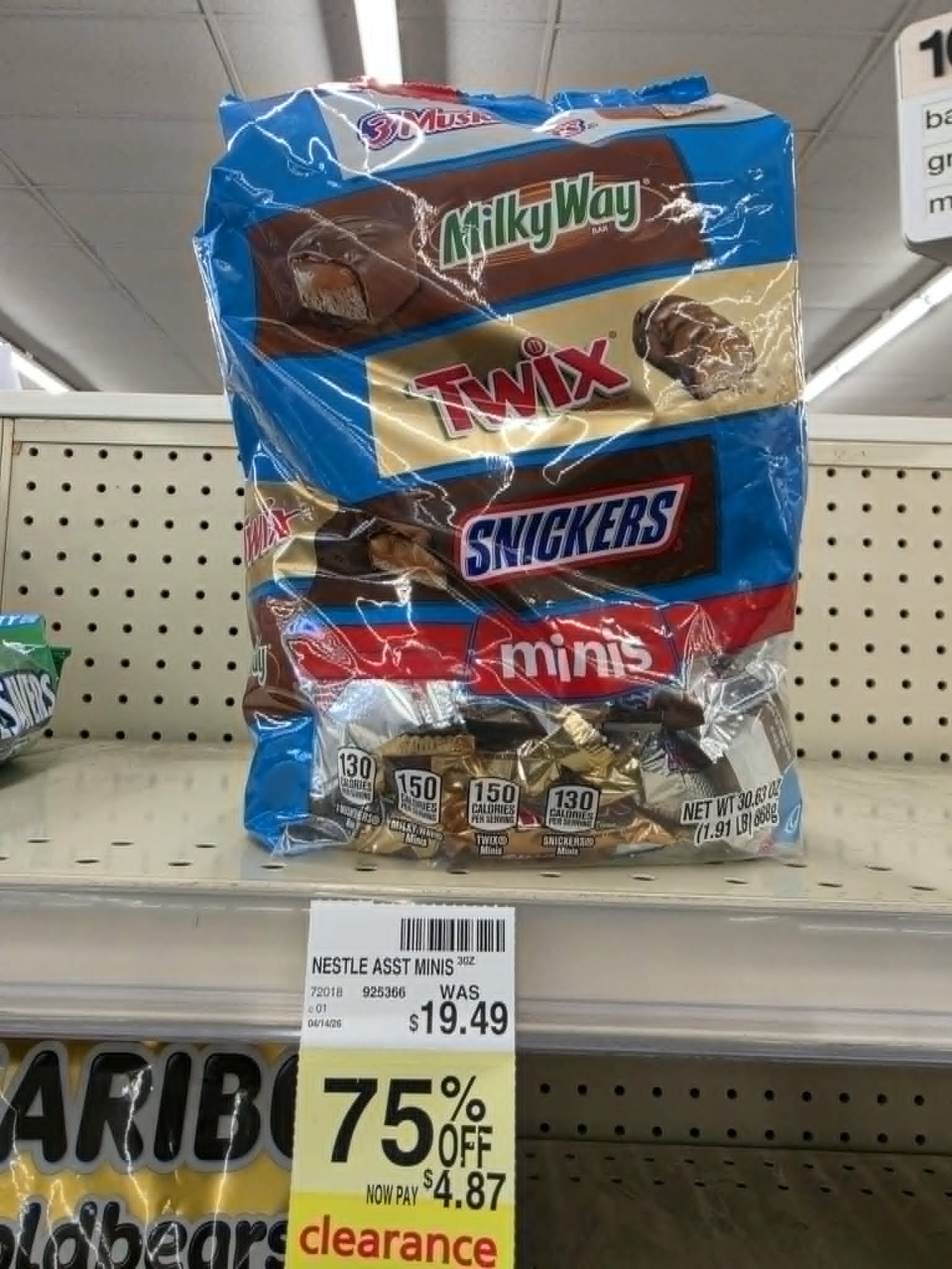 large bag of assorted mini candy bars including Milky Way, Twix, and Snickers on a store shelf with a yellow clearance tag showing 75% off, reduced from $19.49 to $4.87