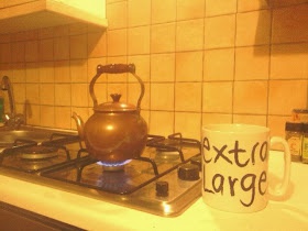 antique small copper kettle on gas cooker next to extra large mug, which it fills comfortably