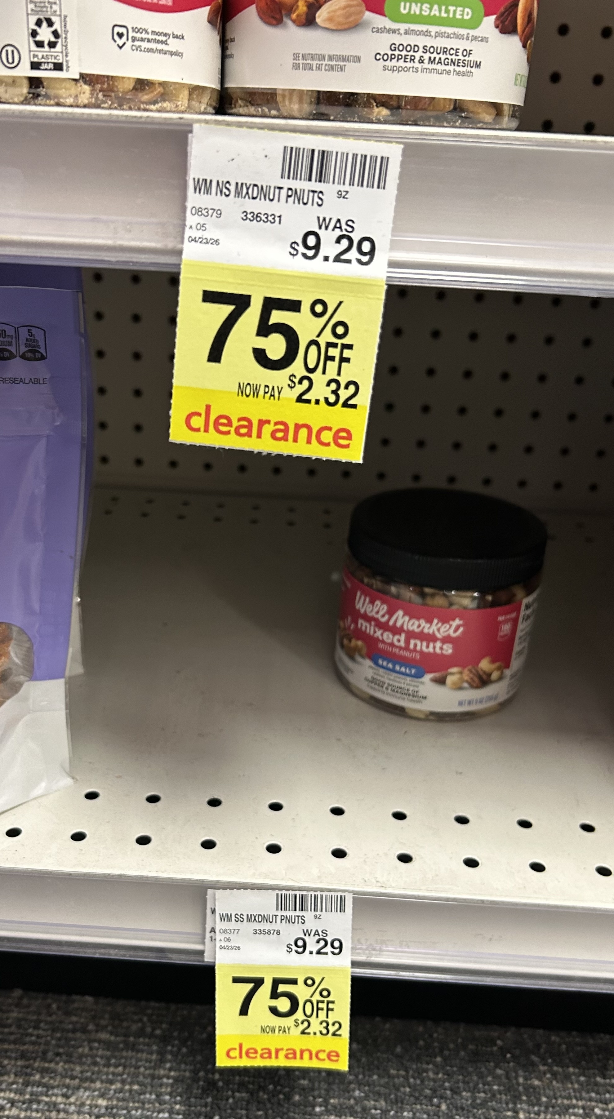 yellow clearance tags on a store shelf showing Well Market mixed nuts discounted 75% off, reduced from $9.29 to $2.32, with a small container of mixed nuts on the shelf nearby